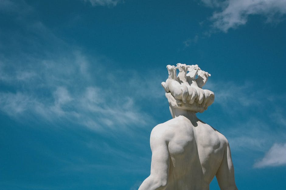 Low-angle view of a Greek statue on a sunny day with a clear blue sky.