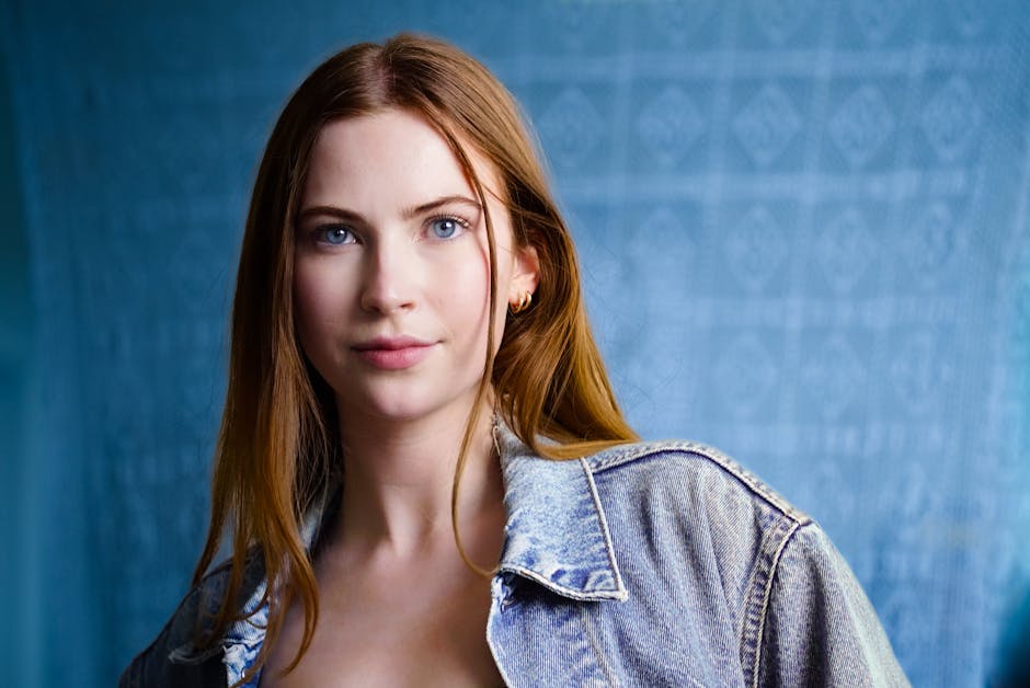 Portrait of a young woman in a denim jacket, with a blue patterned backdrop.
