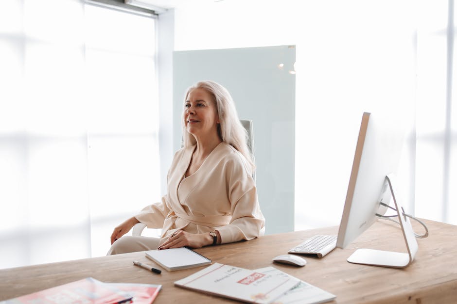 Happy professional woman sitting at a desk with a computer and notes, conveying confidence in a bright office.