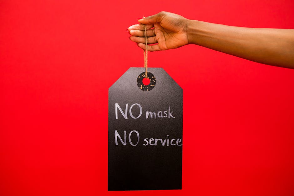 A hand holding a sign with ‘No mask, no service’ message on a red background.