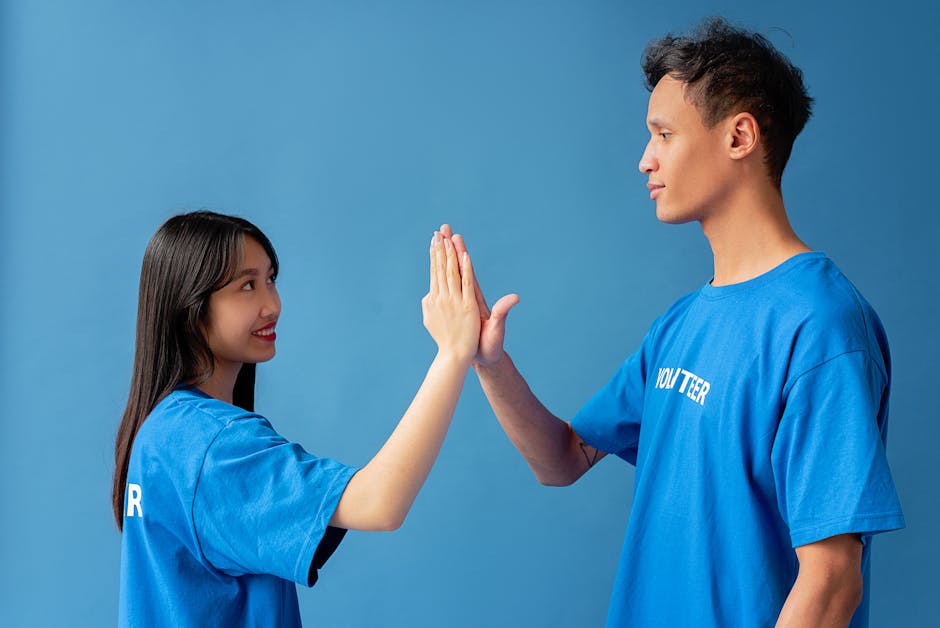 Two young volunteers in blue shirts high-five against a blue background, symbolizing teamwork.