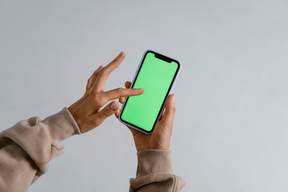Hands interacting with a smartphone showcasing a vibrant green screen for multimedia use.
