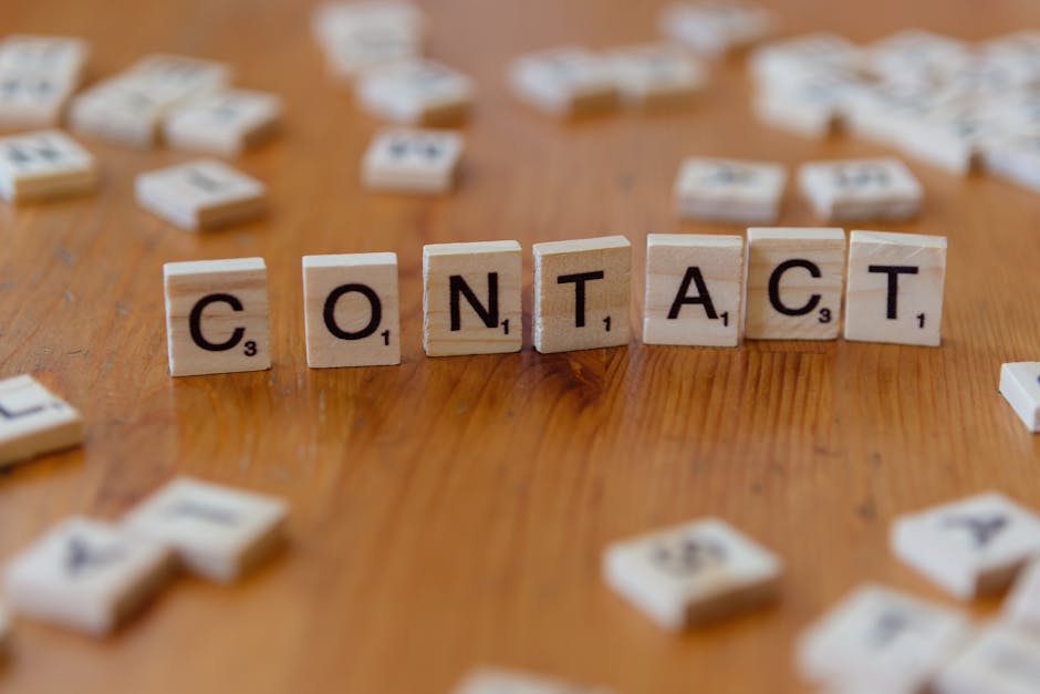 Scrabble letters spelling ‘contact’ on a wooden table surface.