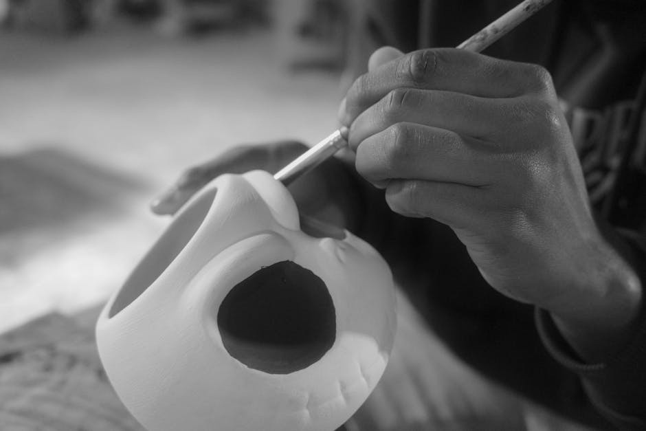 Close-up of hands painting a ceramic skull in black and white, showcasing artistic craftsmanship.