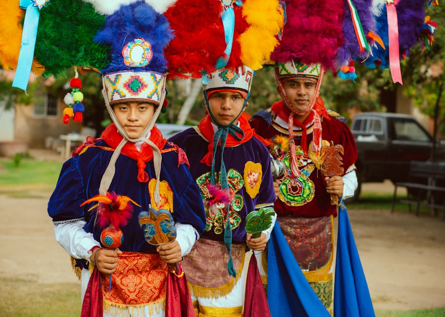 Three men in colorful traditional Mexican costumes with feathered hats and embroidered designs.