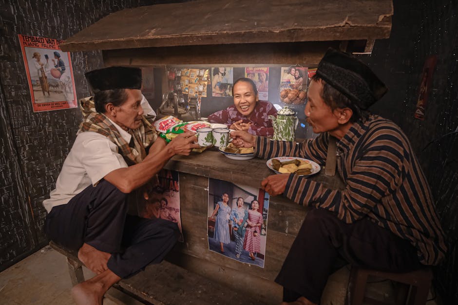 Group of Indonesian people laughing and sharing stories over coffee and traditional snacks at a cozy Warung Kopi (coffee shop), reflecting the warmth of community, friendship, and cultural…
