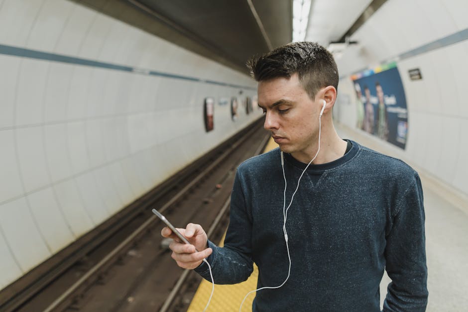 Young man with earphones at subway station using smartphone.