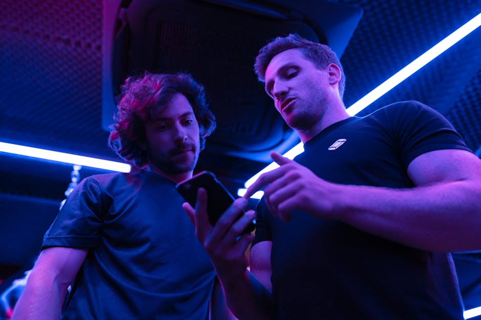 Two men engaging in a focused discussion while looking at a smartphone in a gym setting.