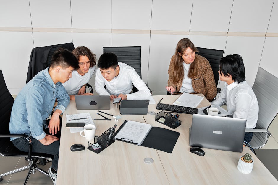 A diverse group of colleagues working together in an office setting with laptops and documents.