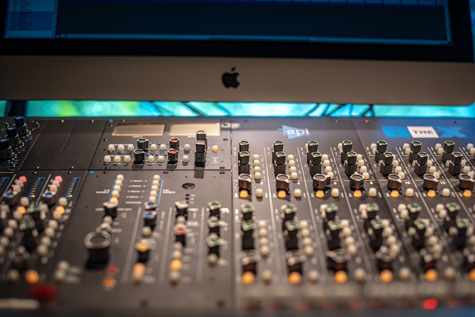 Close-up view of a professional audio mixing console in a modern recording studio with Apple equipment.