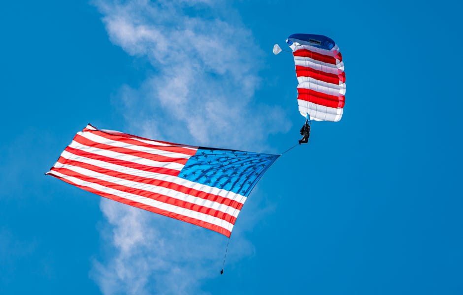 Skydiver parachuting with American flag against clear blue sky in a patriotic display.