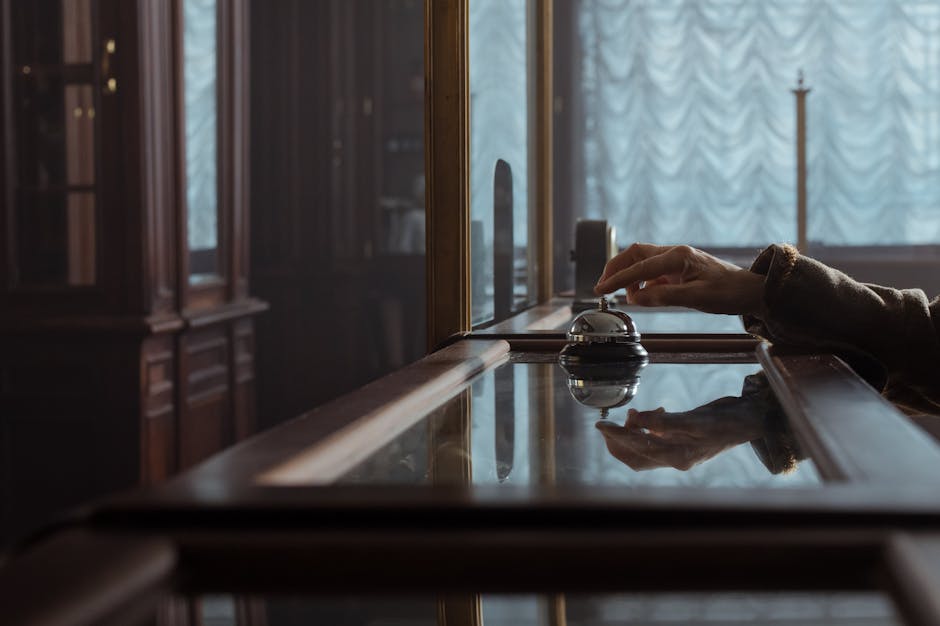 A hand pressing a service bell on an elegant wooden hotel desk, creating a classic atmosphere.