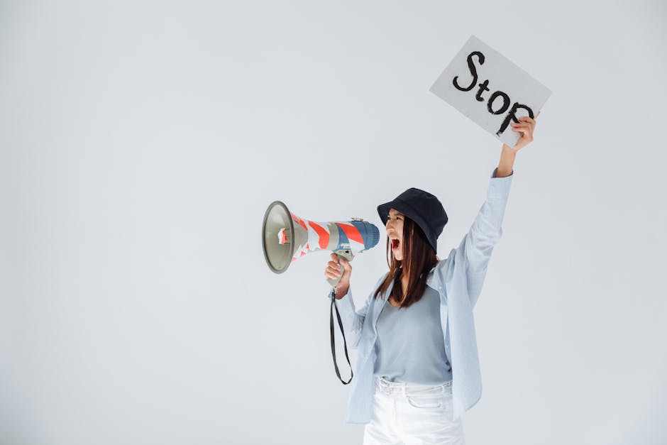 Woman passionately protesting with a megaphone and ‘Stop’ sign in a studio setting.