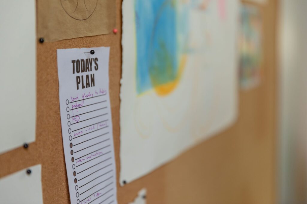 Maintenance reminder card pinned to a corkboard above a hiring lead's planning notes