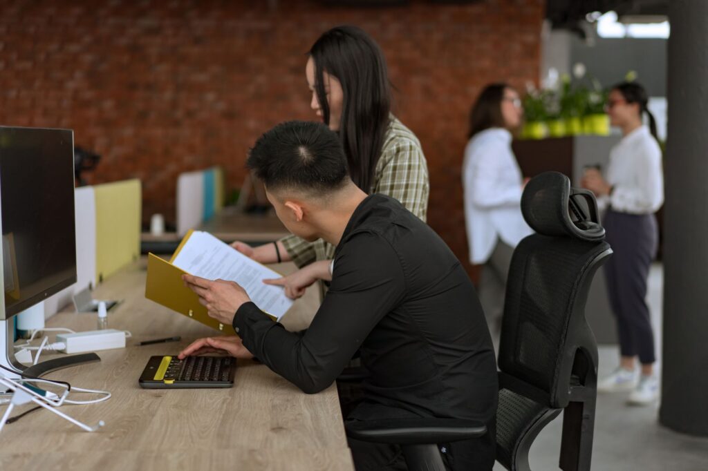 Two developers and a QA lead reviewing build progress at a standing desk with printed status board